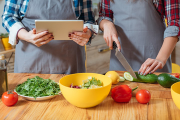 Family leisure in kitchen. Mother and daughter watching online culinary class, making salad with fresh vegetables. Healthy diet.