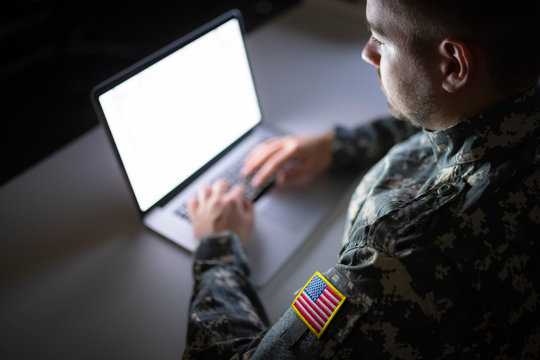 White caucasian soldier in USA military uniform working on the computer at night.