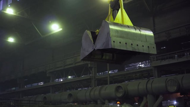 In a dark factory floor a large yellow open two-leaf grab is advanced