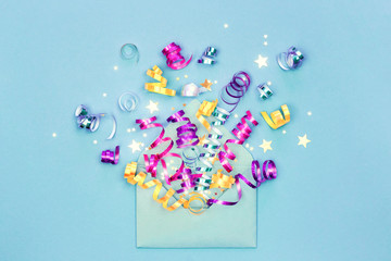 Envelope with party streamers and confetti on blue background. Invitation and greeting card, flat lay. Birthday party explosion concept.
