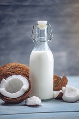 Coconut milk in a bottle with white flesh on a blue wooden background. Organic product used in cosmetology
