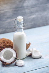 Coconut milk in a bottle with white flesh on a blue wooden background. Organic product used in cosmetology