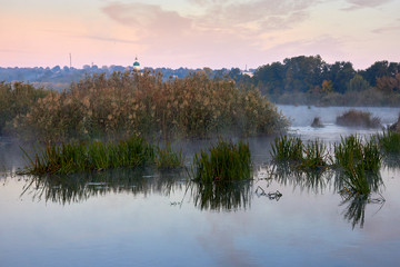 Haze over the river in the early autumn morning. Reeds mist fog and water surface on the river at sunrise