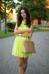 Fototapeta premium Beautiful lady portrait standing in a summer city holding bag