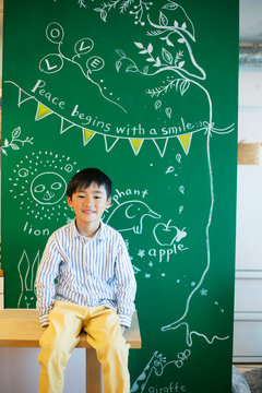 絵の書いてあるボードの前に座る男の子