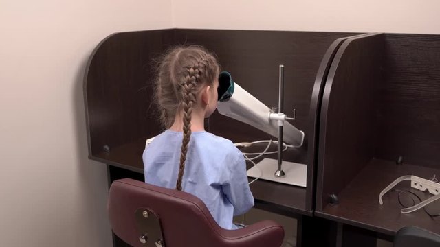 Little caucasian girl sitting on chair during eyesight check-up. Ophthalmological cabinet. Professional ophthalmological equipment usage. Vision testing concept.