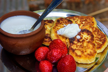 Cottage cheese pancakes/syrniki/curd fritters with fresh strawberries and cream. Traditional Ukrainian and Russian breakfast.
