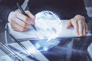 Double exposure of hands making notes with world map hologram and data theme icons. Concept of global computer data.