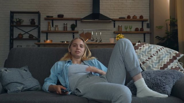 Young woman watching TV at home, sitting on the sofa. Sleepy and tired, yawning. 