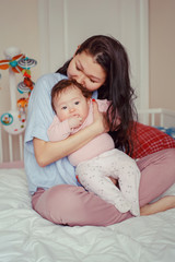 Fototapeta na wymiar Portrait of beautiful mixed race Asian mother kissing touching embracing her cute adorable newborn infant baby. Early development and health care lifestyle concept. Family in bedroom