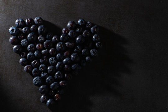 Low key blueberries in a heart shape. Dark and moody intentional light. Modern contemporary stylish healthy food image.