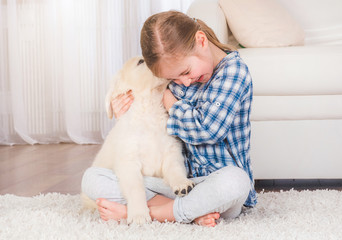 Smiling little girl hugging cute fluffy retriever puppy at home