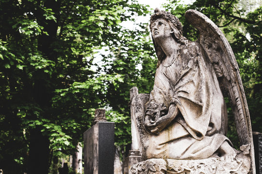Obsolete old stature of angel with cross on burial on cemetery in Lychakiv Cemetery, Lviv