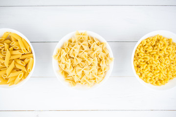 various types of pasta on a white wooden table. Italian cuisine concept, food ingredients. Flat lay. Top view, copy space