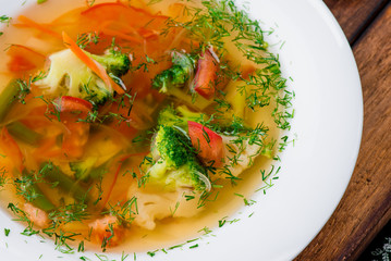 Vegetable broth/soup with broccoli, asparagus, carrots, onions, bell peppers and greens in a white plate on a wooden blue background in a beautiful composition. Close up