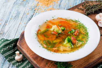 Vegetable broth/soup with broccoli, asparagus, carrots, onions, bell peppers and greens in a white plate on a wooden blue background in a beautiful composition. Close up