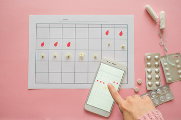 Menstrual cycle. Calendar for the month with marks and a mobile application on the smartphone screen.