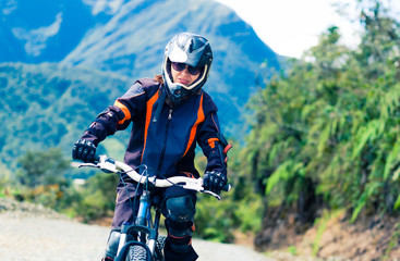 Naklejka premium Girl in special suit and equipment riding a bike on the background of mountains