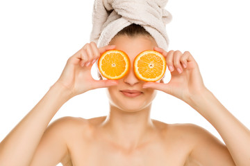 Young beautiful woman with towel on her head holding slices of oranges in front of her eyes on...