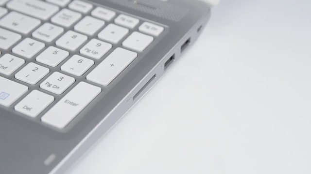 Human hand plugging in an SD media card into the personal laptop computer on white background.