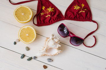 Overhead view of young woman's holidays summer accessories on wooden white background. Swimsuit, sunglasses, lemon, shell, sea pebbles. Vacation soon