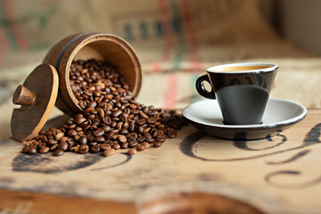 Scattered coffee beans, a cup of espresso, pieces of chocolate with nuts on a wooden board.