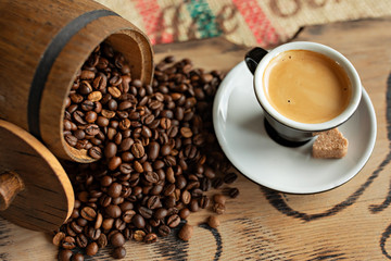 Scattered coffee beans, a cup of espresso, pieces of chocolate with nuts on a wooden board.