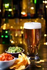 Glass of beer with nachos, tomato salsa and guacamole. Bar bottles in bokeh, high resolution