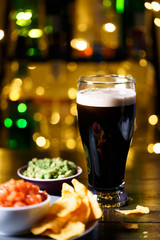 Glass of stout with nachos, tomato salsa and guacamole. Bar bottles in bokeh, high resolution