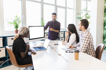 Fototapeta premium Young man discussing market research with colleagues in a meeting. Team of young international professionals having a meeting in conference room looking at documents.