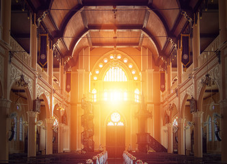 interior view of empty church with wooden bench decorated with flower bouquet, sunlight through...