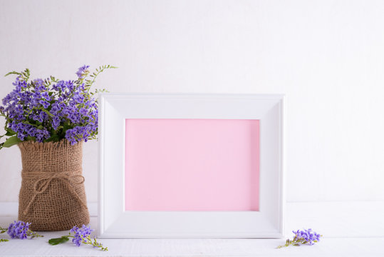 Happy mothers day concept. White picture frame with lovely purple flower in vase on white wooden table.