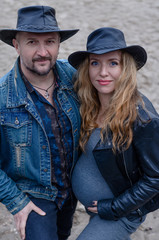 Stylish pregnant couple in cowboy hats outdoors in nature. Beautiful happy woman and her husband are waiting for a baby.