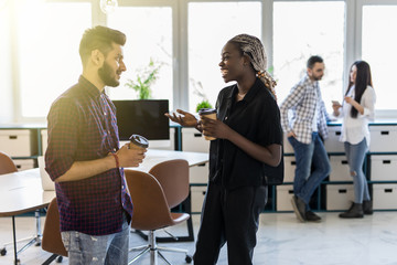 Diverse friends two coworkers standing at office distracted from work take break drink coffee having informal talk. Boss employee planning new project discuss interesting idea companionship concept