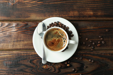 Cup of coffee with spoon and coffee beans on wooden background, space for text and top view