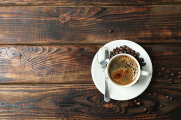 Cup of coffee with spoon and coffee beans on wooden background, space for text and top view