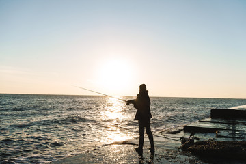 Silhouette of man fisherman wearing coat, holding rod