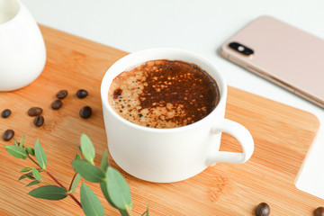 Cutting board with cup of fresh coffee, milk, coffee beans, phone and plant branch on white background, space for text