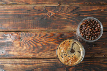 Glass of fresh coffee and coffee beans on wooden table, space for text and top view