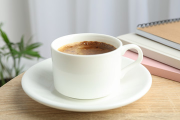 Cup of coffee and notebooks on wooden table against light background with plant, space for text and closeup