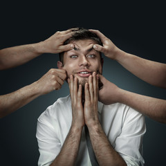 Fototapeta premium A male model surrounded by hands like his own thoughts on dark background. A young man doubts, can't choose the right decision and decide. Concept of mental problems, troubles in work, indecision.