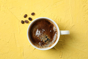 Cup of coffee with frothy foam and coffee beans on color background, top view and space for text. Coffee time accessories