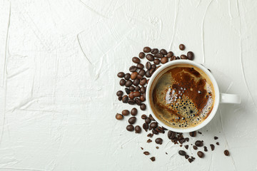 Cup of coffee with frothy foam and coffee beans on white background, top view and space for text. Coffee time accessories