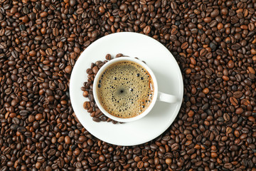 Cup of coffee with frothy foam on beans background, top view and space for text. Coffee time accessories