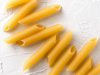 Raw pasta as food background. Italian Penne Rigate Macaroni Pasta on textured white background....