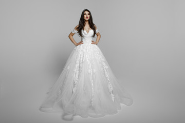Fototapeta na wymiar Luxury bride in long white wedding princess dress. Charming bride in a magnificent wedding dress. Bride in luxurious suites. Female models poses standing with hands on her waist
