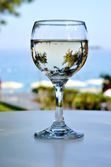 Glass of white wine on table on the beach. Beautiful view with sea and pines