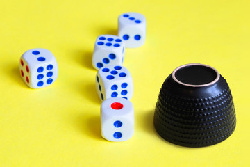 White dice for the game are located on a yellow background next to a black china cup.