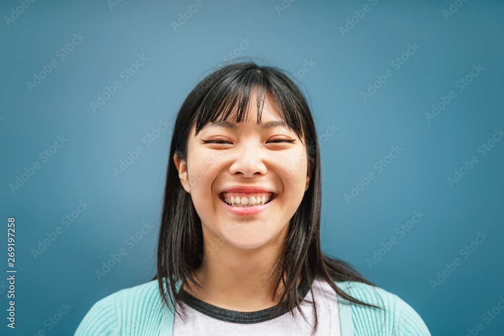 Wall mural Portrait of young Asian girl smiling at camera - Happy Chinese woman having fun posing against blue background - Teen, trendy, millennial generation and youth people lifestyle