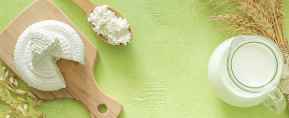 Shavuot concept - dairy products and wheat on green wood background, copy space
